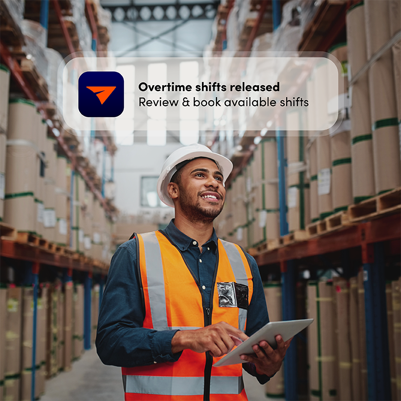 Smiling warehouse worker with Elevate app notification for overtime shift, demonstrating dynamic staff scheduling for fast gap filling.